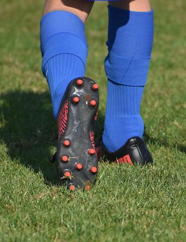 student's legs showing blue high-socks and cleats walking in the turf